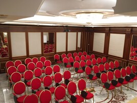 A conference room with rows of red chairs, a chandelier, and wooden paneled walls.