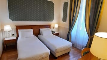Een hotelkamer met twee enkele bedden, een houten bureau, een stoel, een telefoon en een lamp.