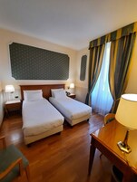 Een hotelkamer met twee enkele bedden, een houten bureau, een stoel, een telefoon en een lamp.