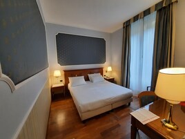 A hotel room with a large bed, two bedside tables with lamps, a wooden desk, and a chair.