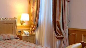 Quarto de hotel com cama, mesa de cabeceira com abajur, telefone e uma cadeira.