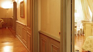 A hallway with wooden flooring and a marble border. There is a door leading to a room with a bed and a chair. - Andreola Central Hotel (Milan)