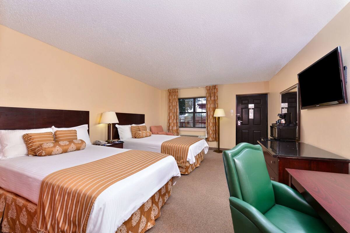A hotel room with two beds, a desk, a chair, a television, and a window with curtains.