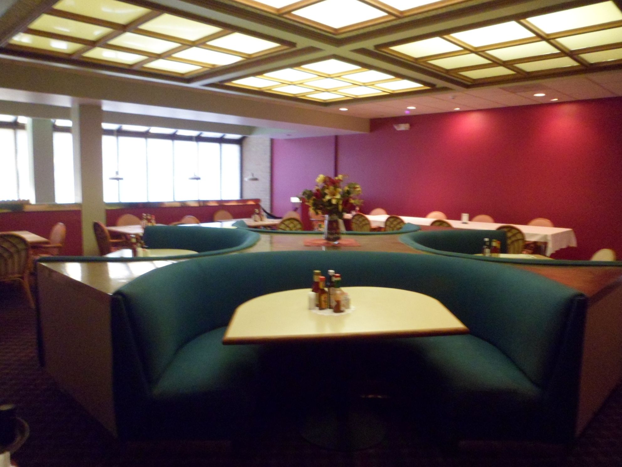 Un restaurant amb seients a cabines i taules, un arranjament floral central i un sostre amb un dibuix geomètric.