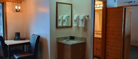 Habitación de hotel compacta con comedor, kitchenette, baño con tocador y armario de madera.