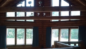 Una cabaña de madera de varios niveles con un dormitorio en la buhardilla, ventanas amplias y un ventilador de techo.