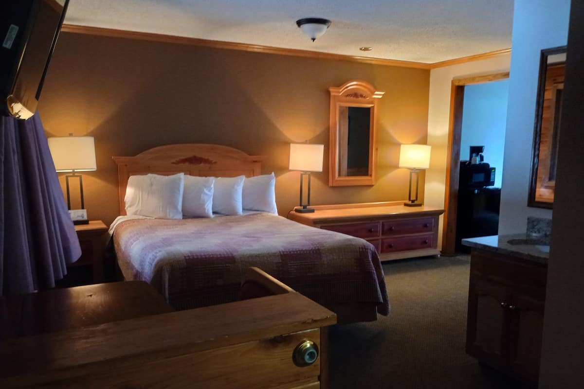 A hotel room with a wooden bed, two bedside tables with lamps, a dresser, a mirror, and a coffee machine in the corner.
