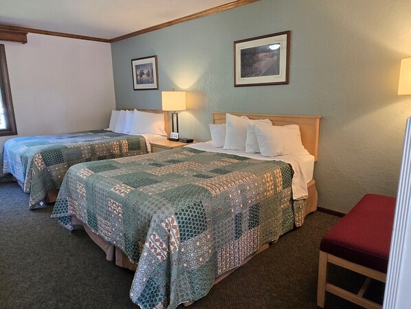 A hotel room with two beds, a nightstand, a lamp, and two framed pictures on the wall. - Centerstone Resort Lake-Aire (Tomahawk)