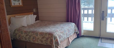 A bedroom with a bed, a door leading outside, and a framed picture on the wall.