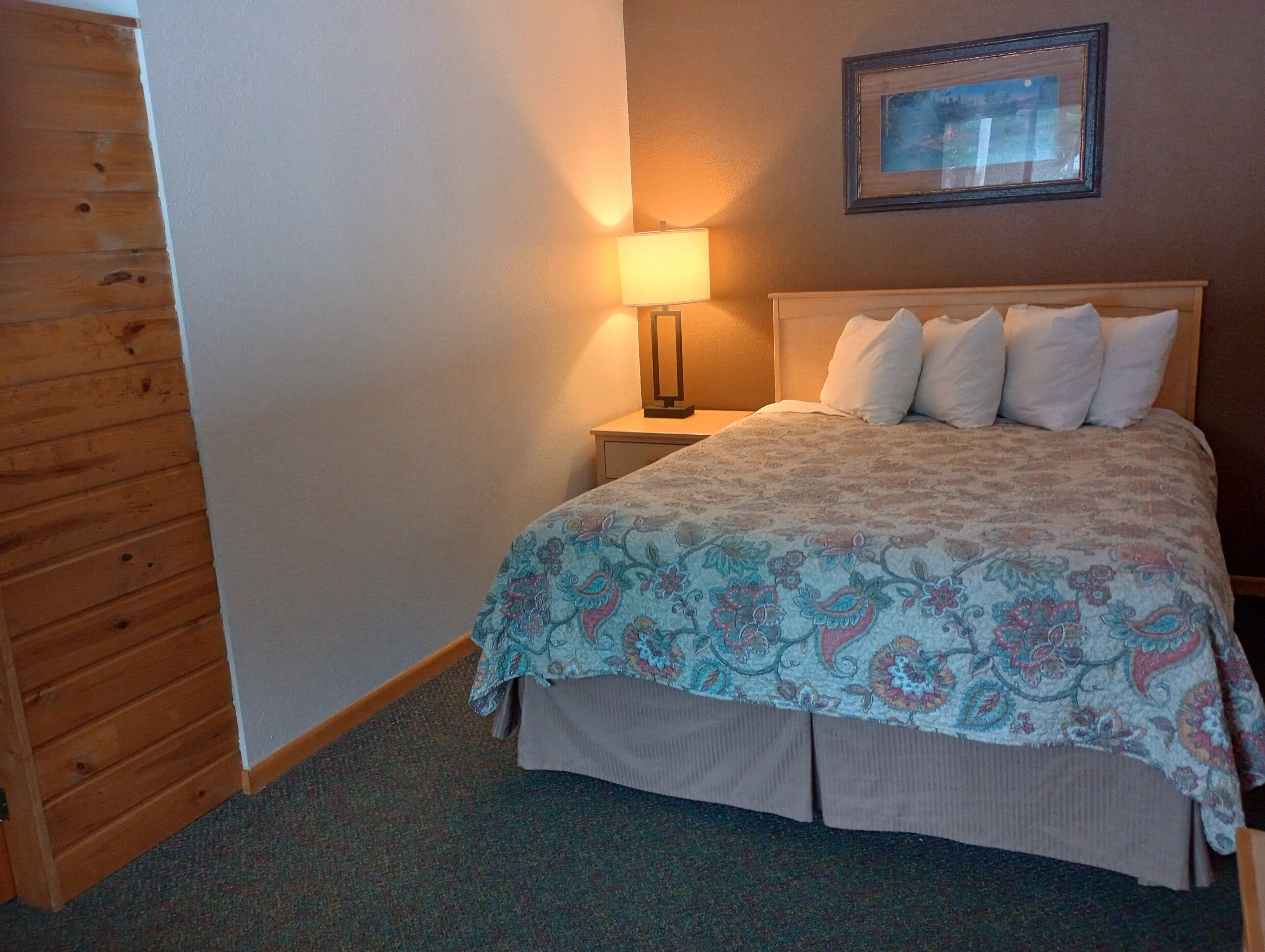 A bedroom with a bed, a nightstand, a lamp, and a framed picture on the wall.