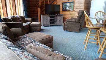 A cozy log cabin interior with a sofa, armchairs, a small table, and a television.