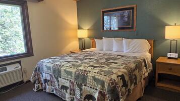 A bedroom with a large bed, two bedside tables with lamps, a window with a view, and a wall-mounted picture.