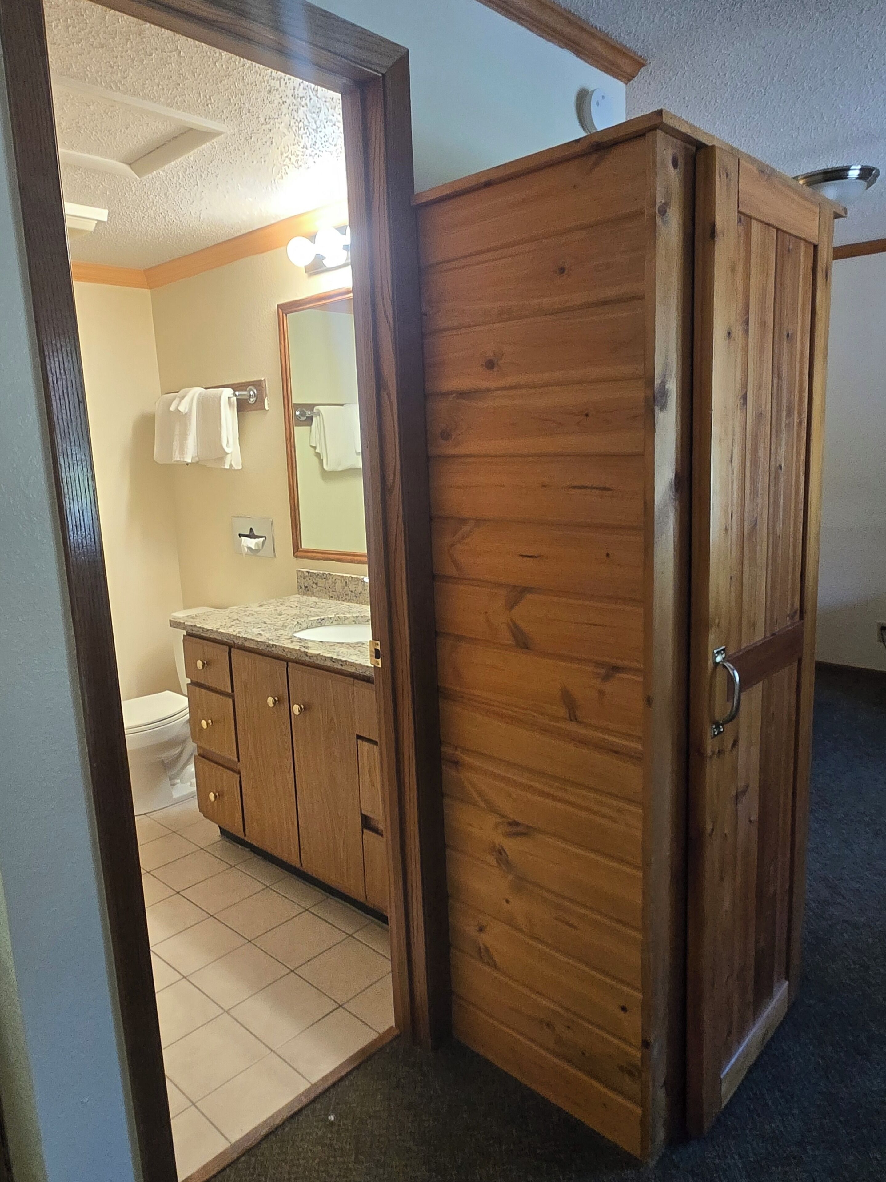 A bathroom with a wooden cabinet, a toilet, and a mirror.