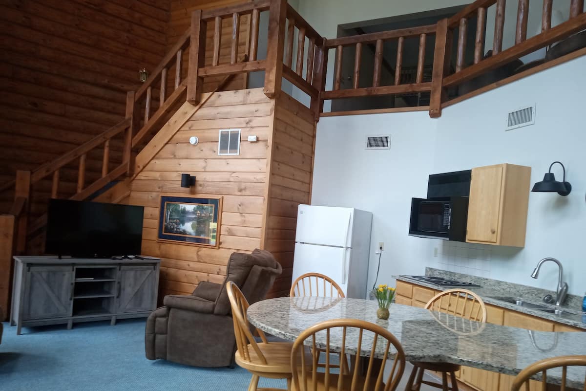 A cozy cabin interior with a dining area, kitchen, and a wooden staircase.