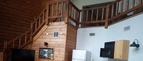 A cozy cabin interior with a dining area, kitchen, and a wooden staircase.
