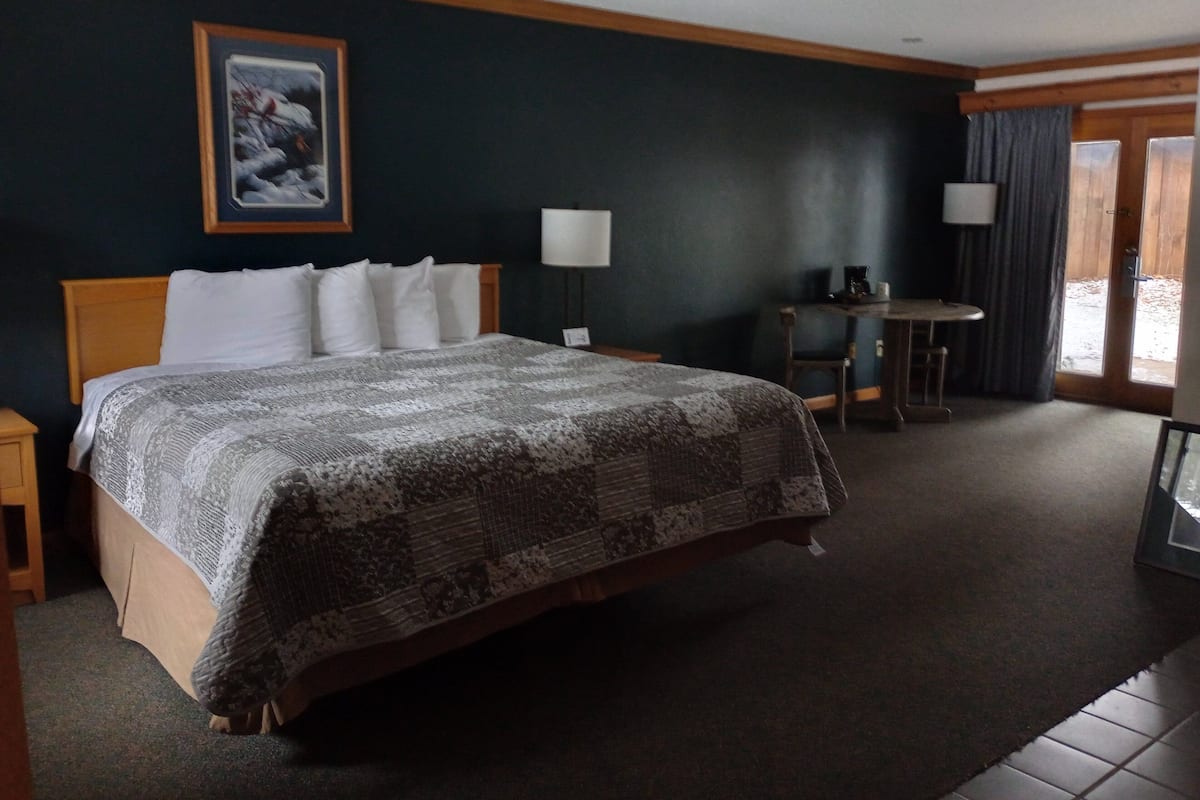 A hotel room with a large bed, a desk, a chair, a lamp, and a window with curtains.