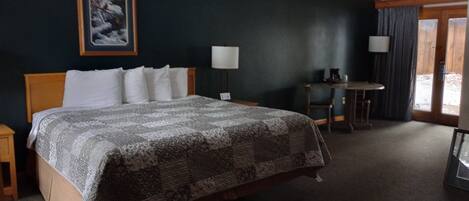 A hotel room with a large bed, a desk, a chair, a lamp, and a window with curtains.