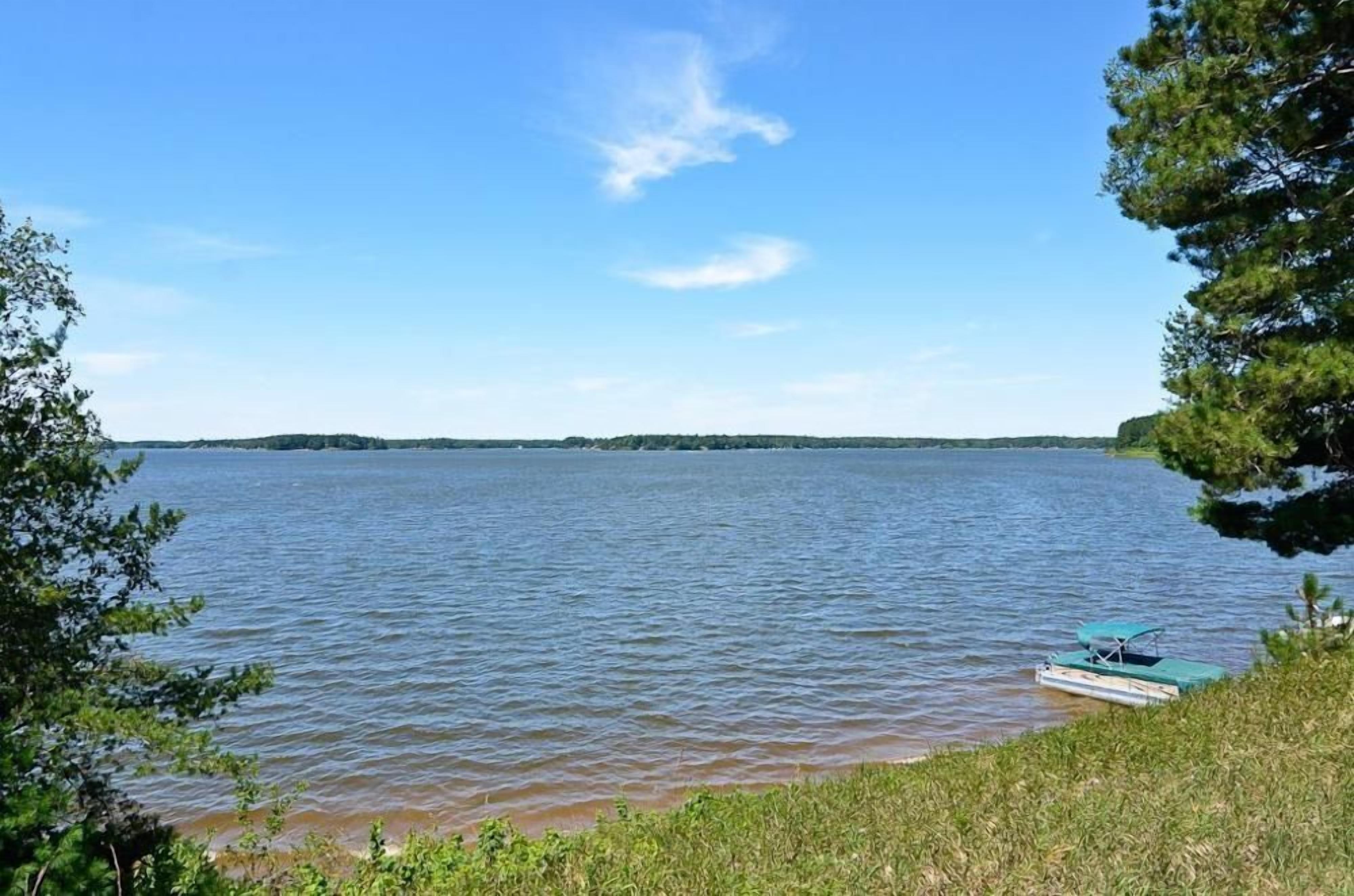 Un lac paisible, avec une petite barque amarrée sur la rive, entouré d’arbres et sous un ciel dégagé.