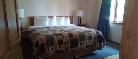 Habitación de hotel con una cama grande, dos mesitas de noche, una ventana con cortinas y una puerta.