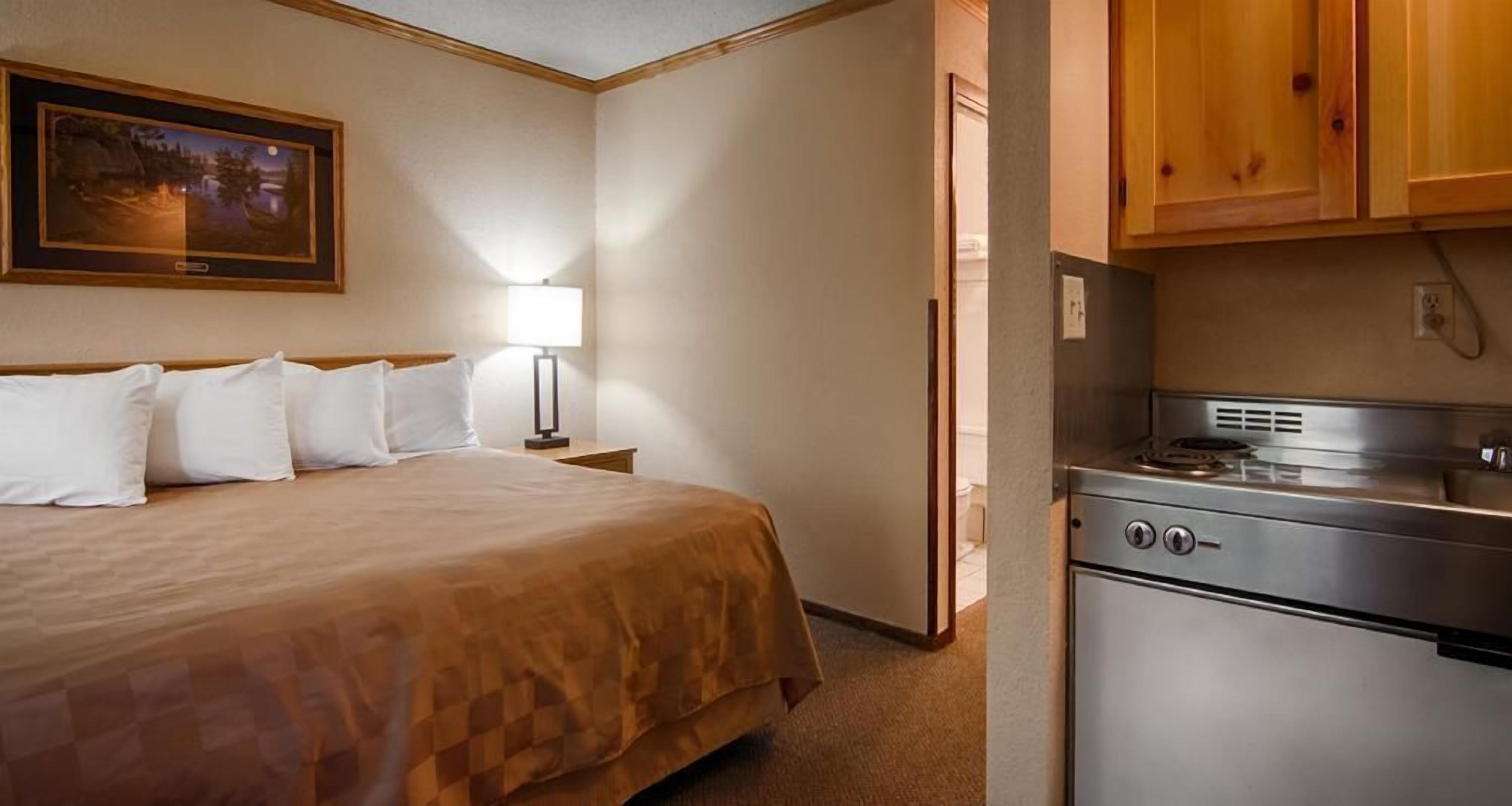 Ein Hotelzimmer mit Bett, Nachttisch, Lampe, einem Gemälde und einer Küchenzeile.