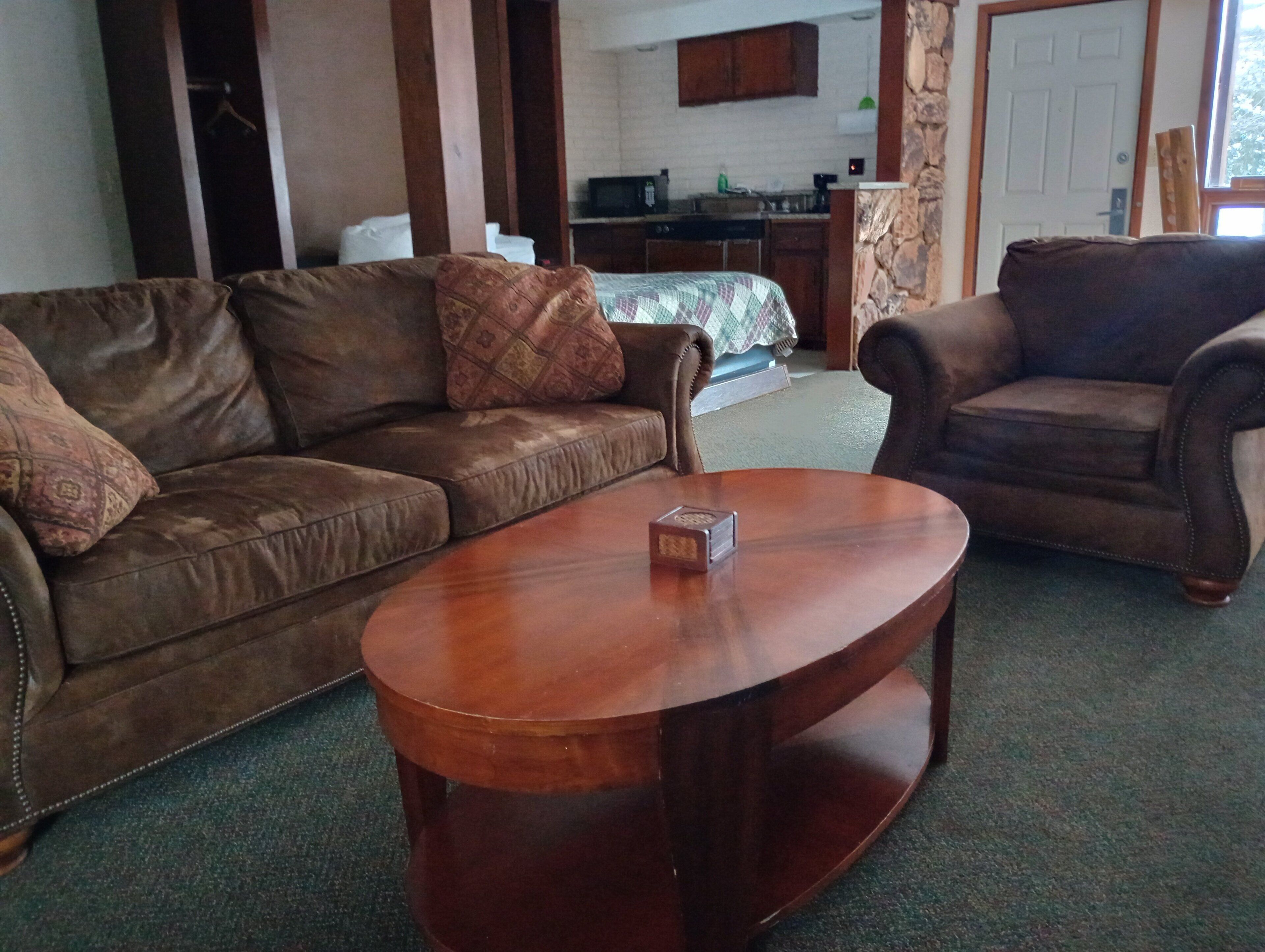 A living room with a brown leather sofa, a wooden coffee table, and a kitchen in the background.