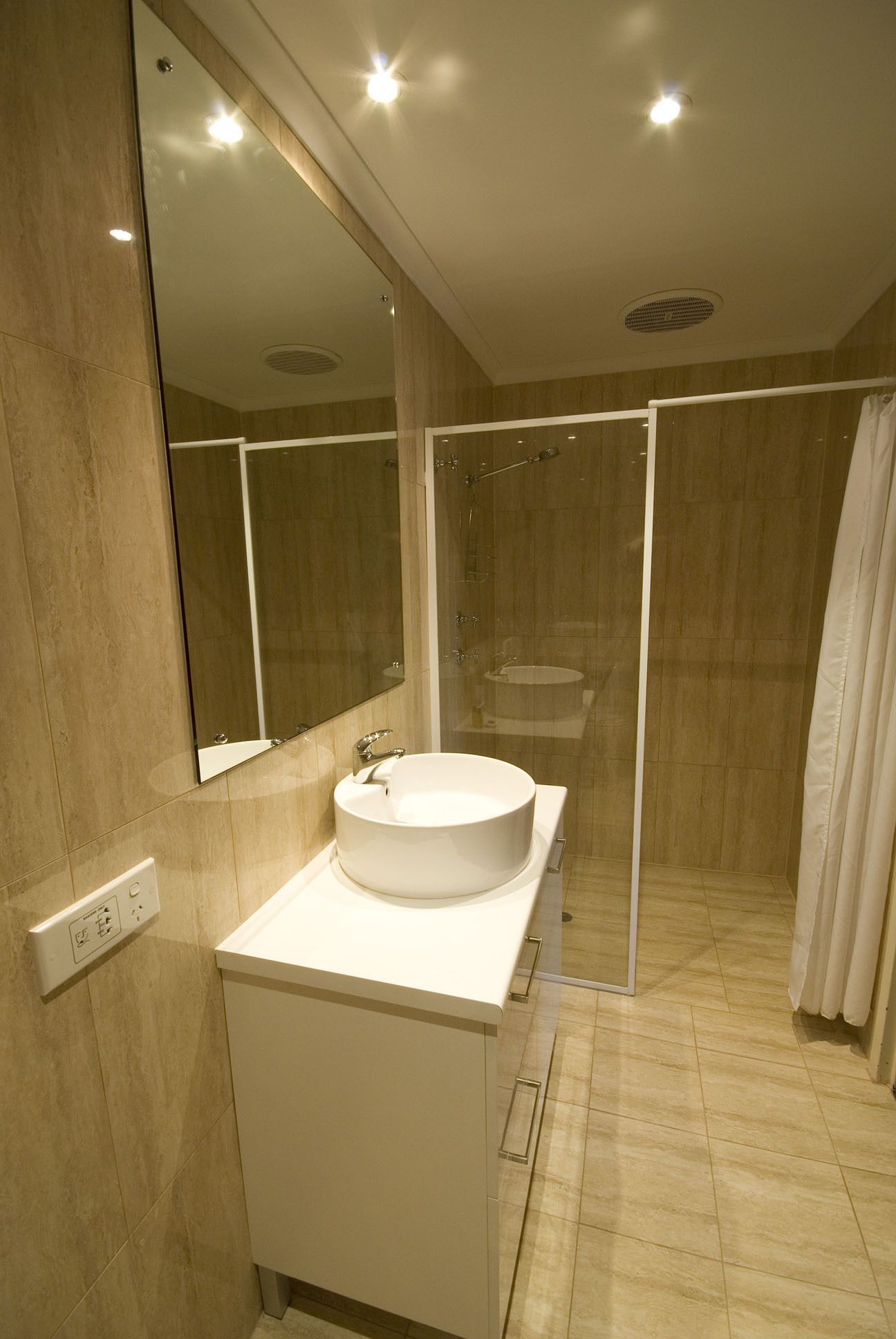 Un baño moderno con un espejo grande, un lavamanos redondo y una ducha con mampara de vidrio.