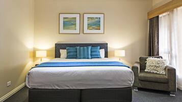 A hotel room with a large bed, two bedside lamps, a chair with a throw pillow, and two framed pictures on the wall.