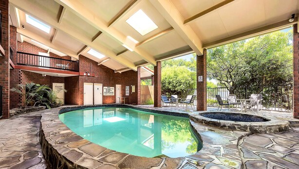 A swimming pool with stone tiles, a covered patio area, and a view of trees.