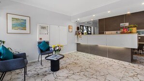 A reception area with a marble floor, two armchairs, a coffee table with flowers, a reception desk, and a framed picture on the wall.