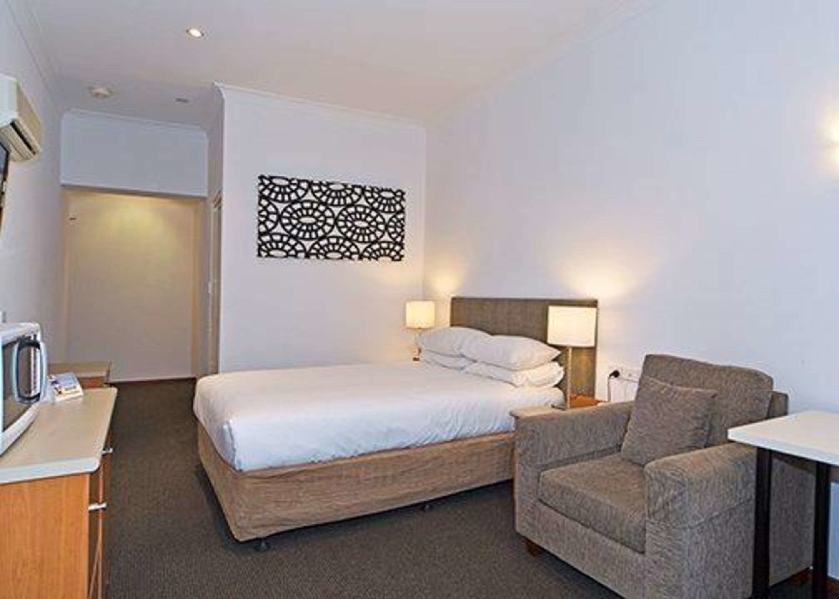 Ein Hotelzimmer mit einem Einzelbett, einem Sessel, einem Schreibtisch und einer Wanddekoration.