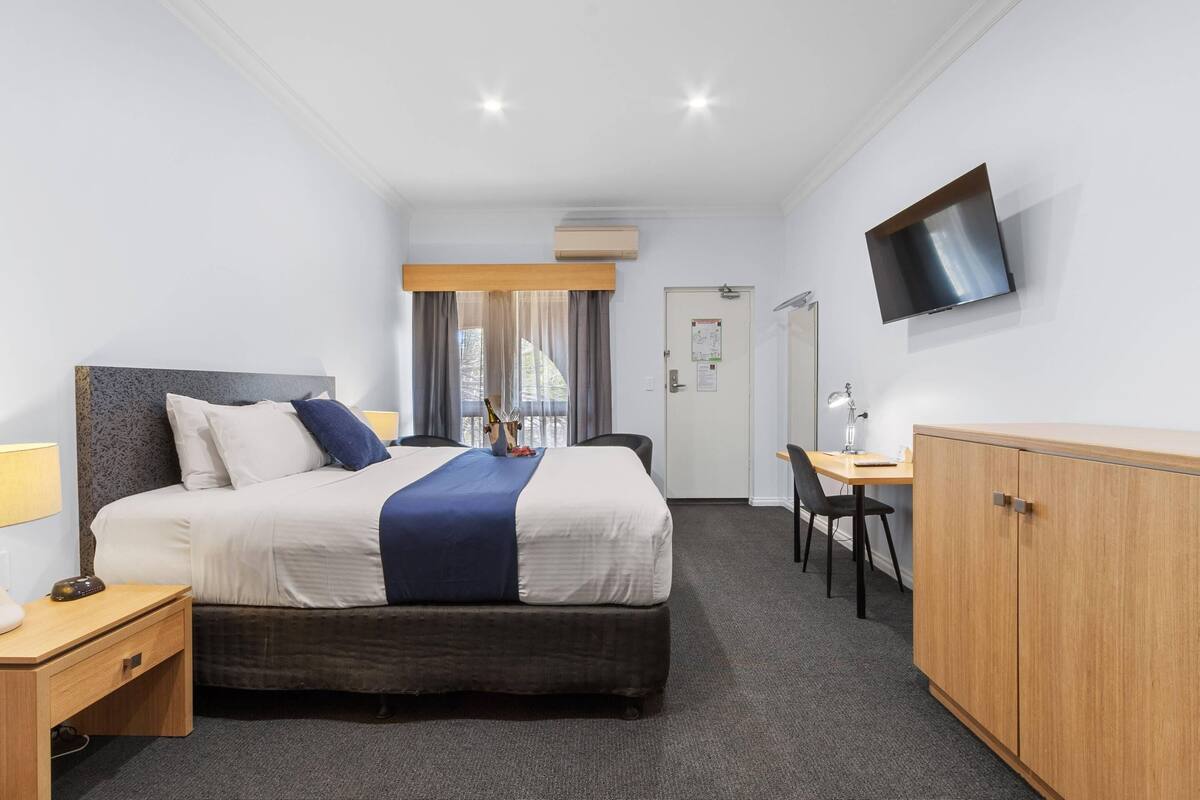 Quarto de hotel com cama, escrivaninha, televisão e guarda-roupa.