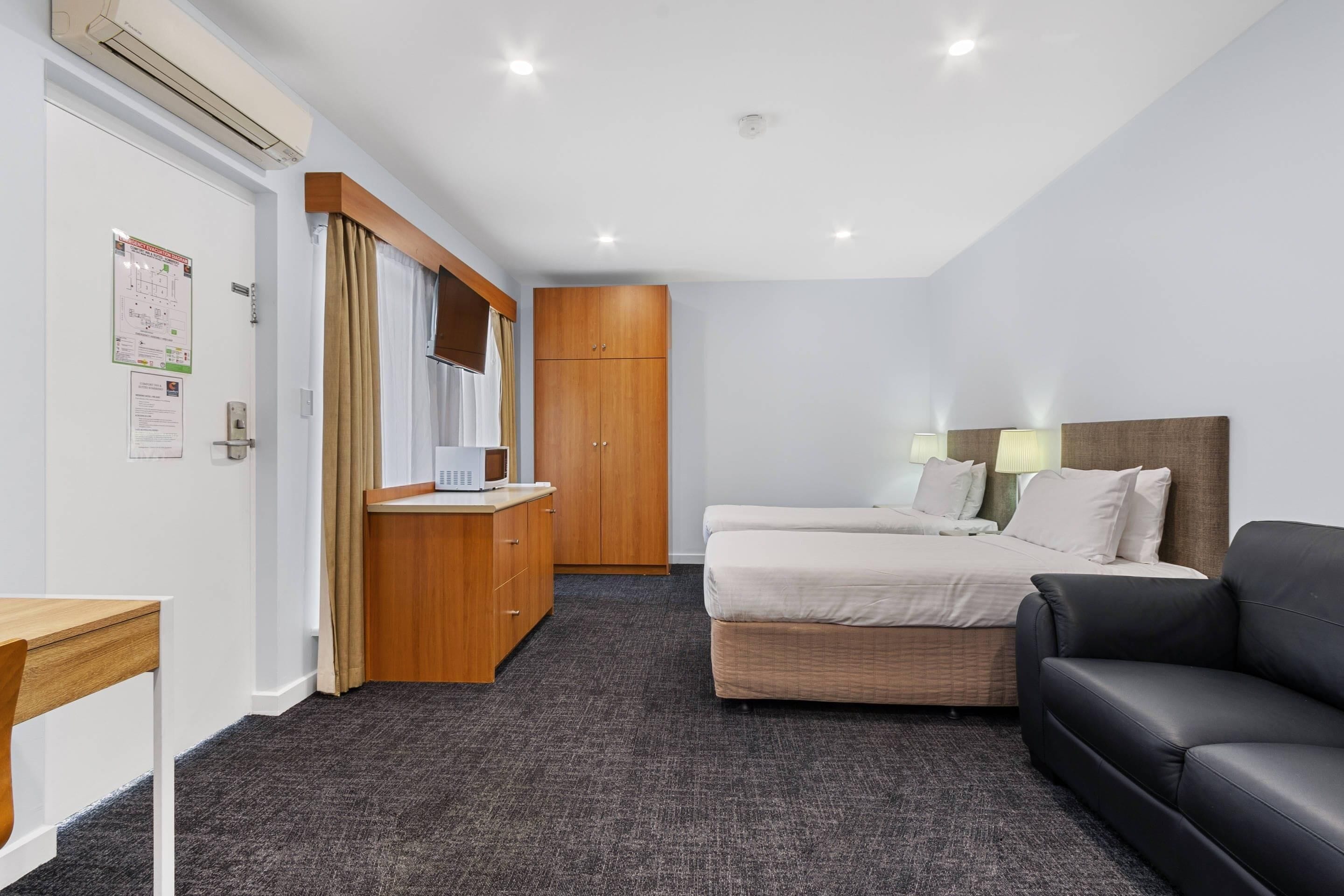 Habitación de hotel con cama, escritorio, armario, sofá y aire acondicionado instalado en la pared.