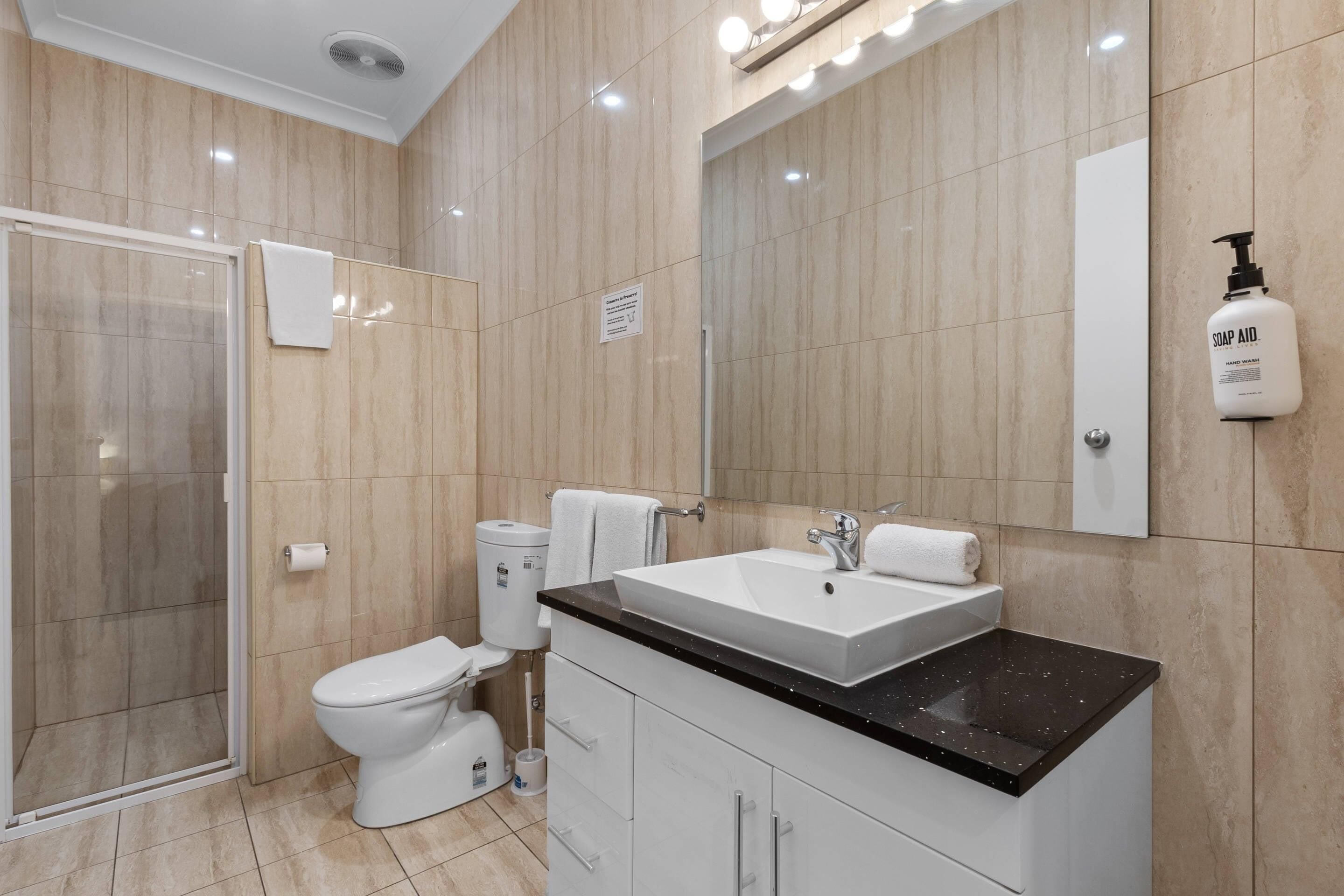 A modern bathroom with a glass shower enclosure, a toilet, a sink with a mirror, and a soap dispenser.
