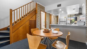 A modern kitchen with a wooden staircase, a dining area with a round table and chairs, and a view of the outside.