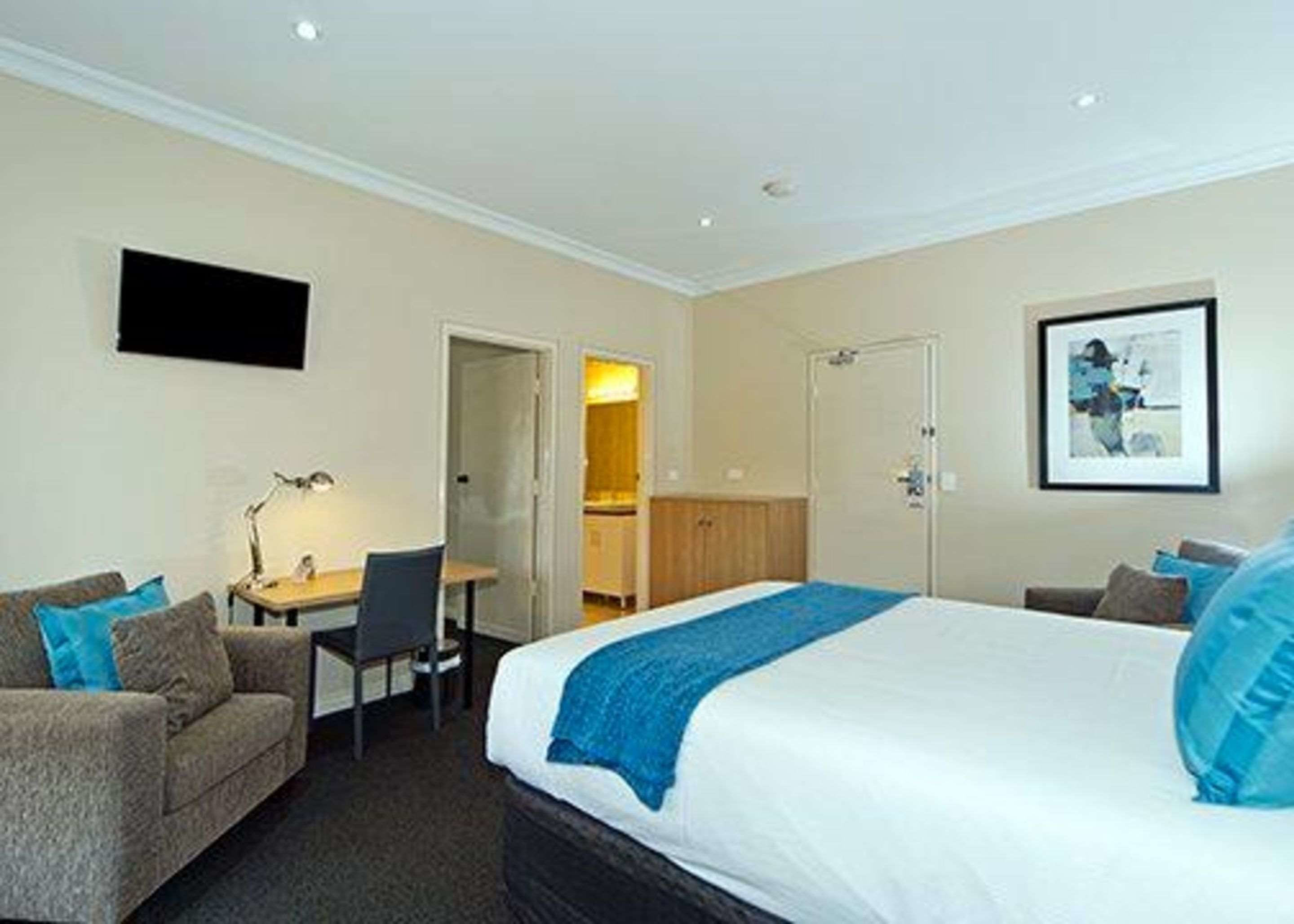 A hotel room with a bed, a desk, a chair, a sofa, and a television on the wall.