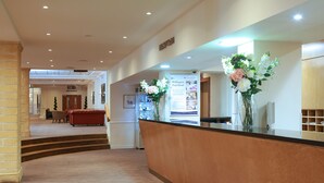 Zona de recepción de hotel con un mostrador, un sofá rojo y una escalera que sube a otro piso.