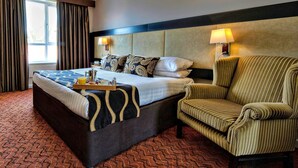 Una habitación de hotel con una cama grande, una silla, una bandeja con alimentos para el desayuno y dos lámparas de noche.