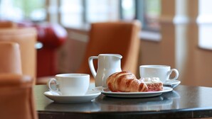 Una mesa con un croissant, dos tazas y una jarra, probablemente en una cafetería.
