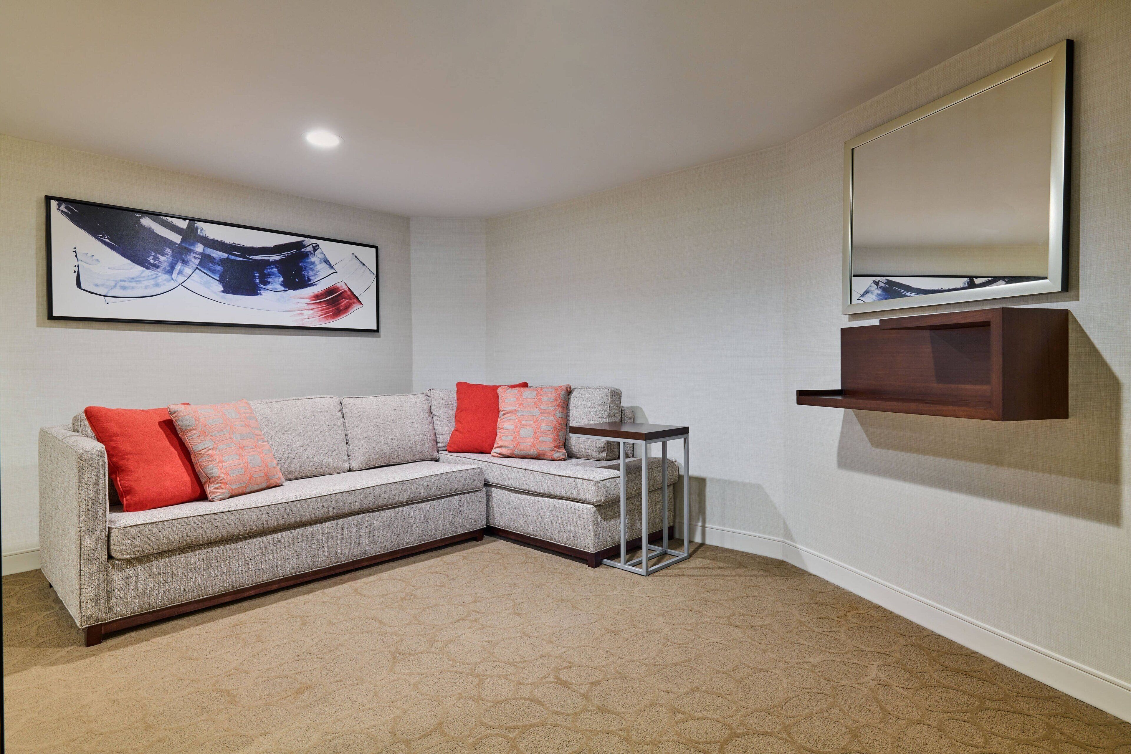 A corner living room with a sectional sofa, a small side table, a large abstract painting, and a mirror on the wall.
