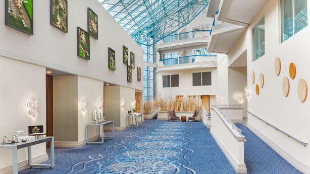 A hotel lobby with a blue carpet, artwork on the walls, and a glass ceiling. -  Delta Hotel Philadelphia Airport (Philadelphia)