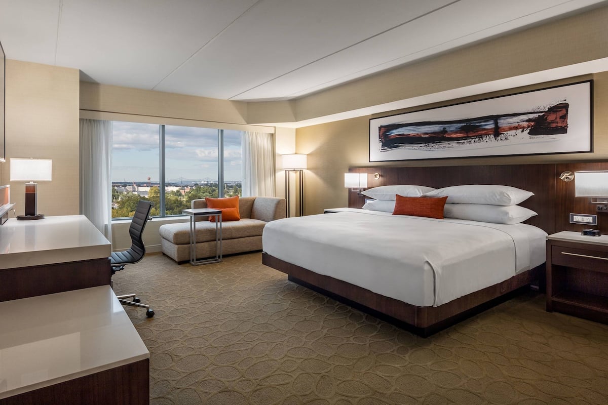 A hotel room with a large bed, a desk, a chair, and a view of the city.