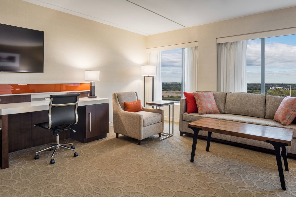 A hotel room with a desk, office chair, sofa, and a view of the outdoors.