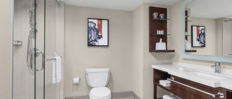 Un baño moderno con ducha de vidrio, inodoro blanco y tocador con espejo.