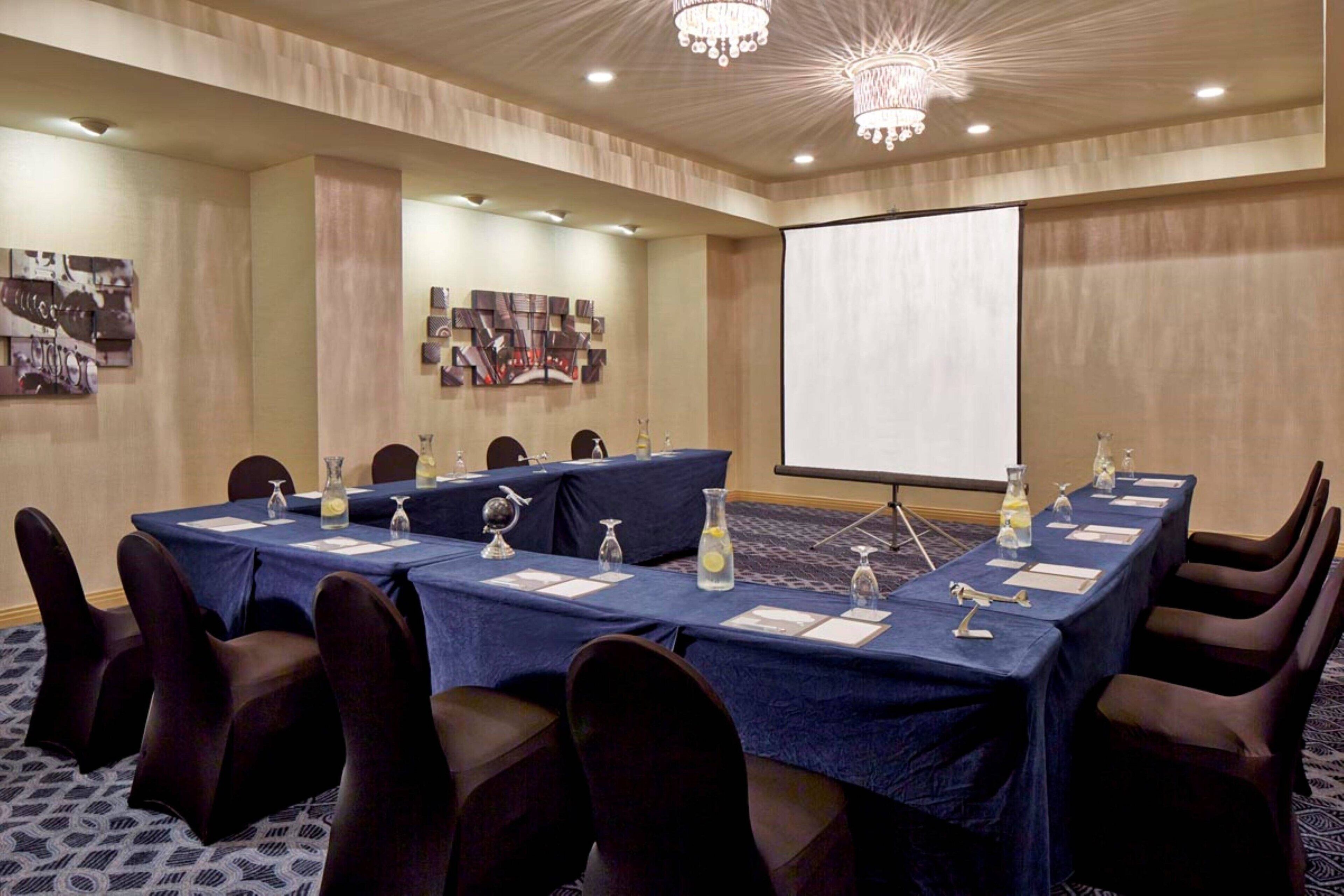 Un salón de conferencias con una larga mesa, sillas, una pantalla de proyector y una araña.