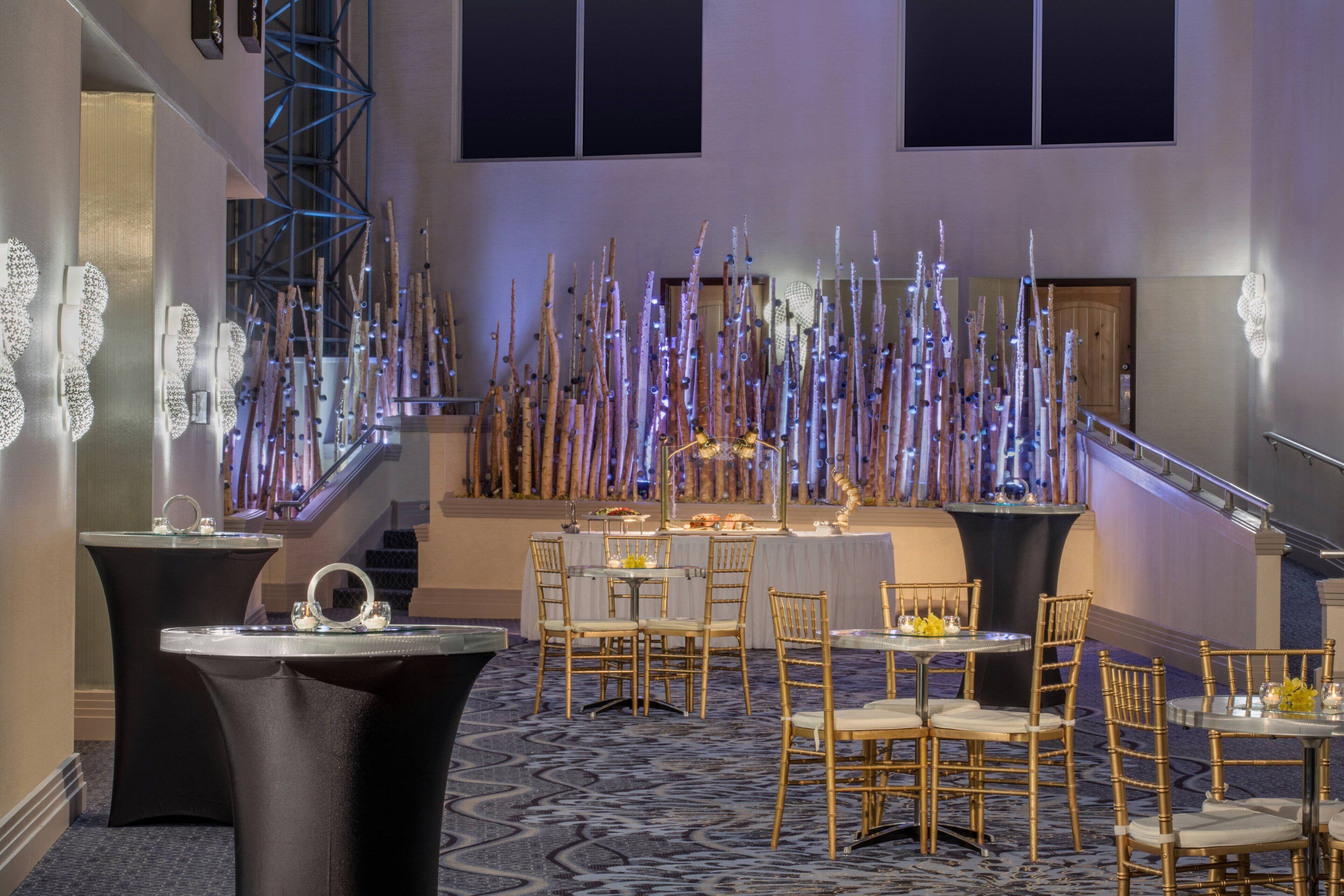 A spacious hotel lobby with a grand staircase, multiple dining tables, and a decorative light installation.