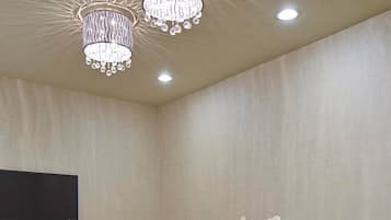 A conference room with a long table, white chairs, a flat-screen TV, and a chandelier.