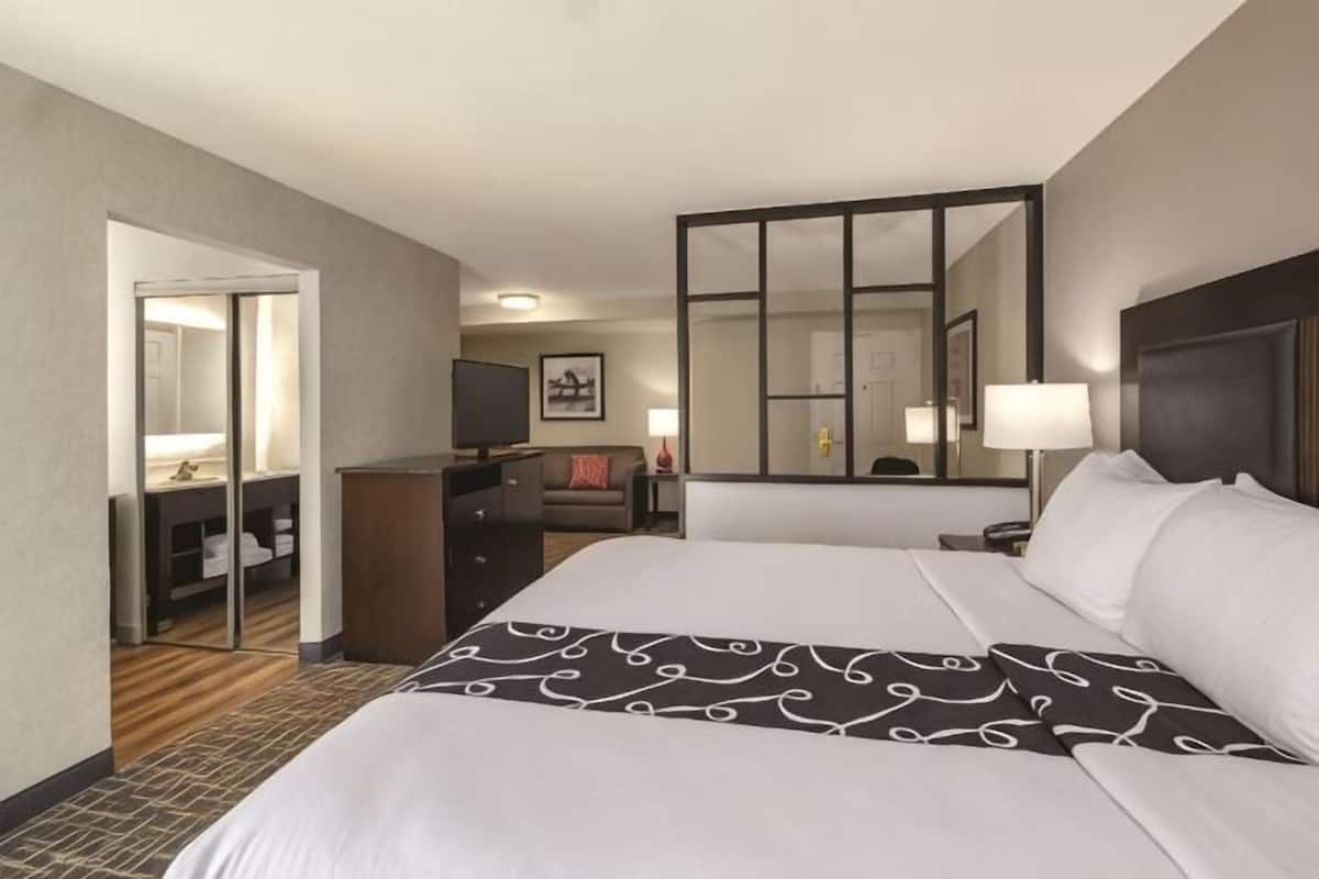 A hotel room with a large bed, a desk, a chair, a television, a mirror, and a door leading to a bathroom.