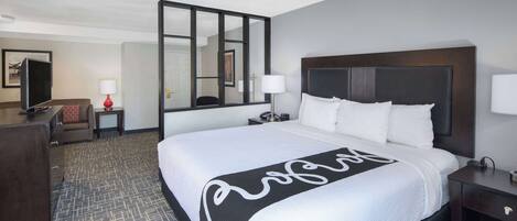 A hotel room with a large bed, a desk, a chair, a TV, and a mirror.