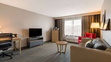 Habitación de hotel con sofá, televisión, escritorio con silla, una mesita redonda y un sillón rojo.