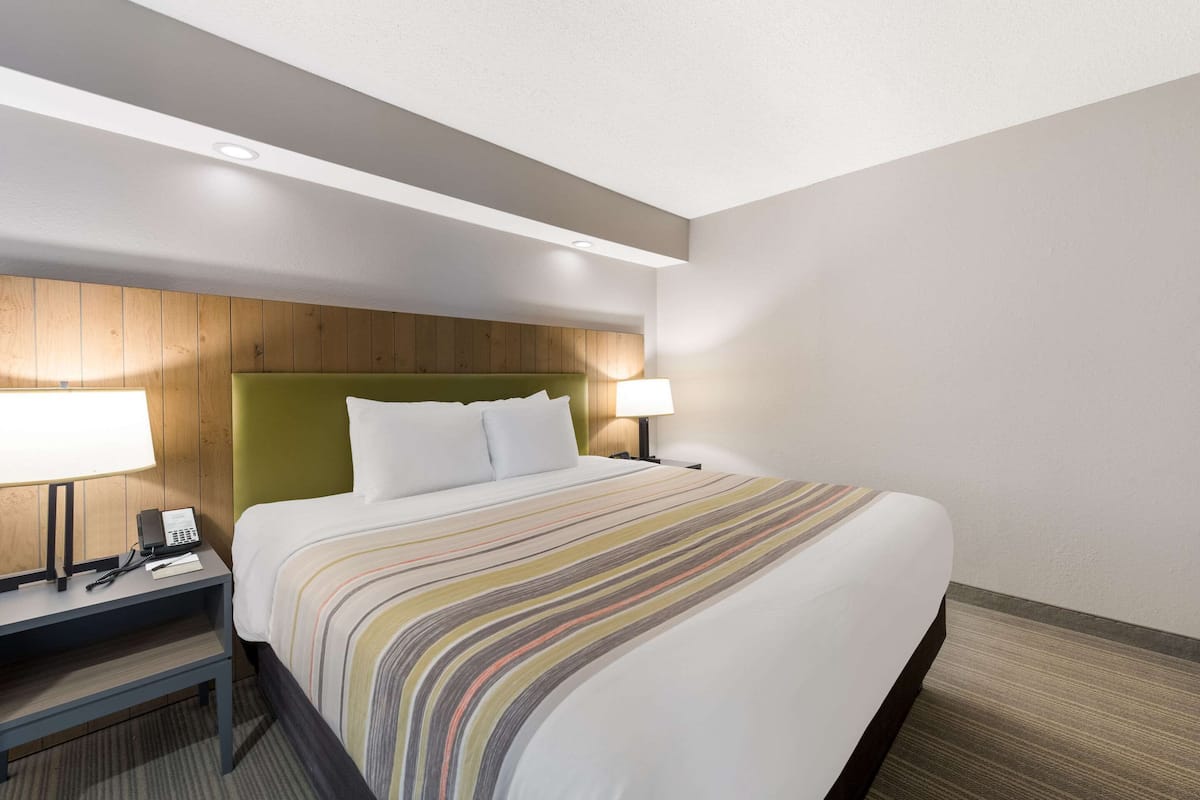 A hotel room with a large bed, a wooden headboard, a nightstand with a lamp, and a phone.